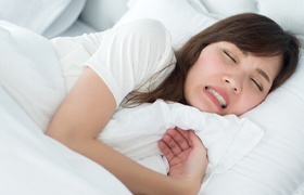 A young woman lying in bed and grinding and clenching her teeth