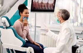 A woman using a cold pack on her jaw while listening to her dentist talk about TMJ Disorder