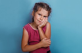 A little girl holding her cheek in pain