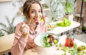 Smiling woman eating salad at home