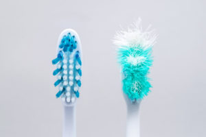 Two blue toothbrushes side-by-side, one new & one with frayed bristles