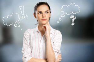 Woman in white blouse with her finger to her cheek as she thinks