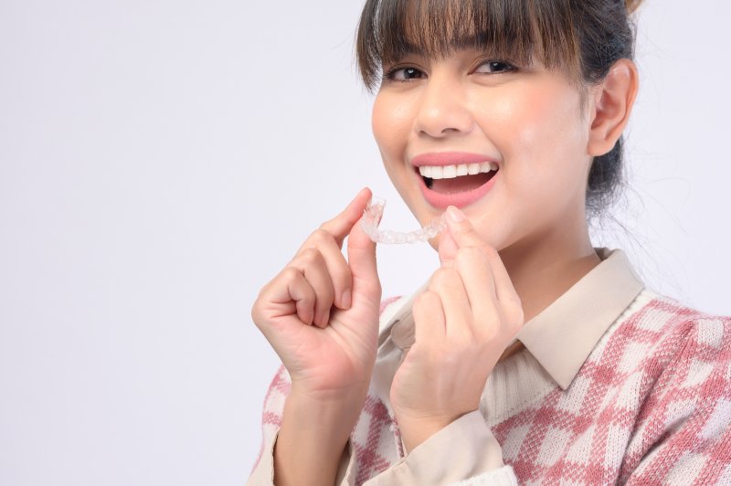 person holding Invisalign aligner and smiling